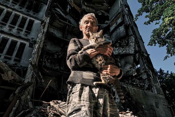 A Ukrainian man and his cat stand outside their destroyed home in Kharkiv in 2022