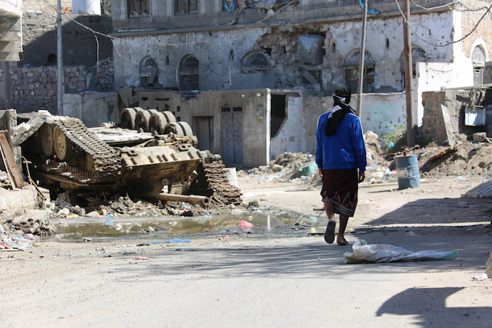 A Yemeni walks past a tank destroyed in the city of Taiz